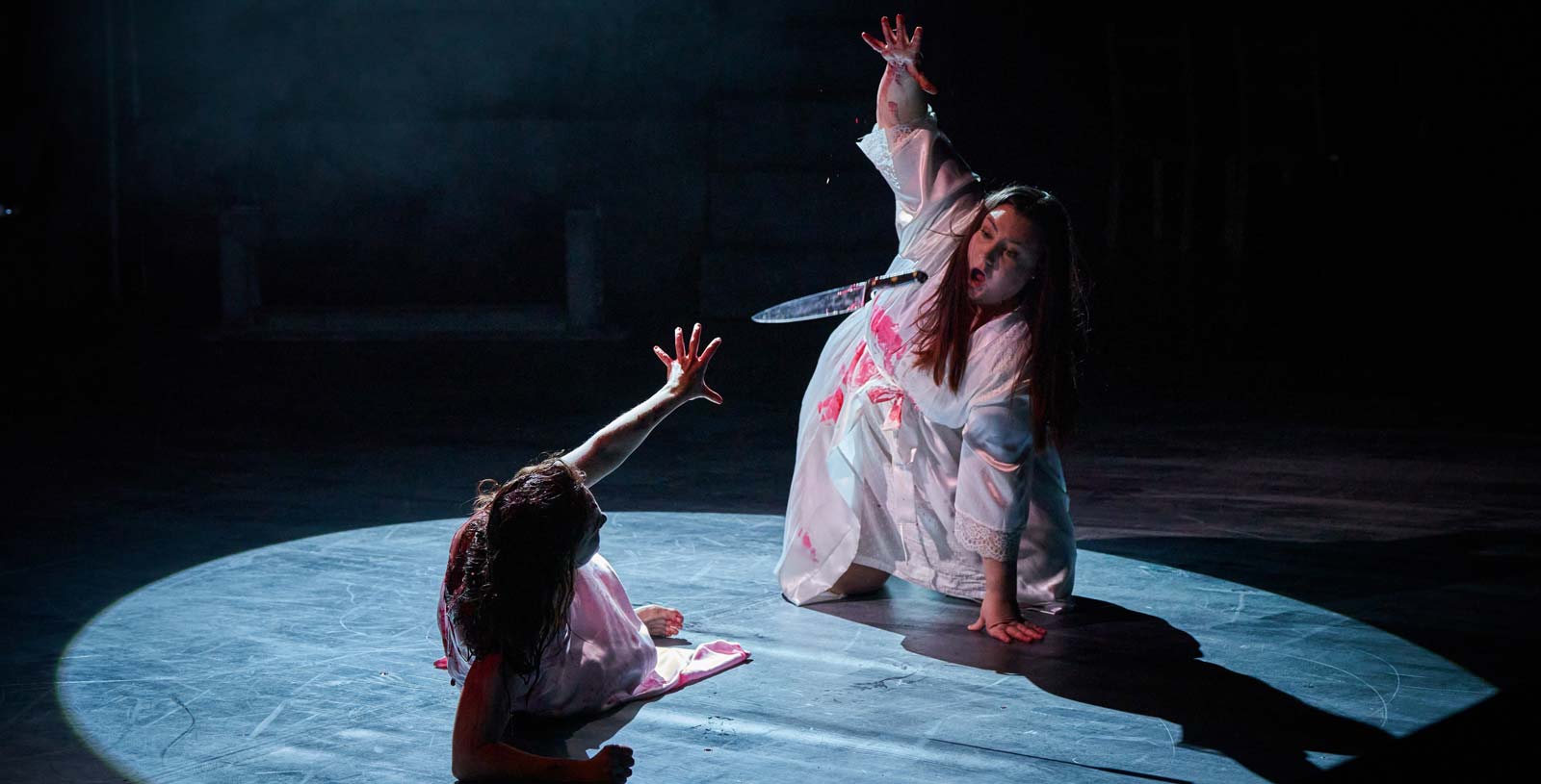 Production of the play Carrie, with one female character throwing a bloodied knife at another female character