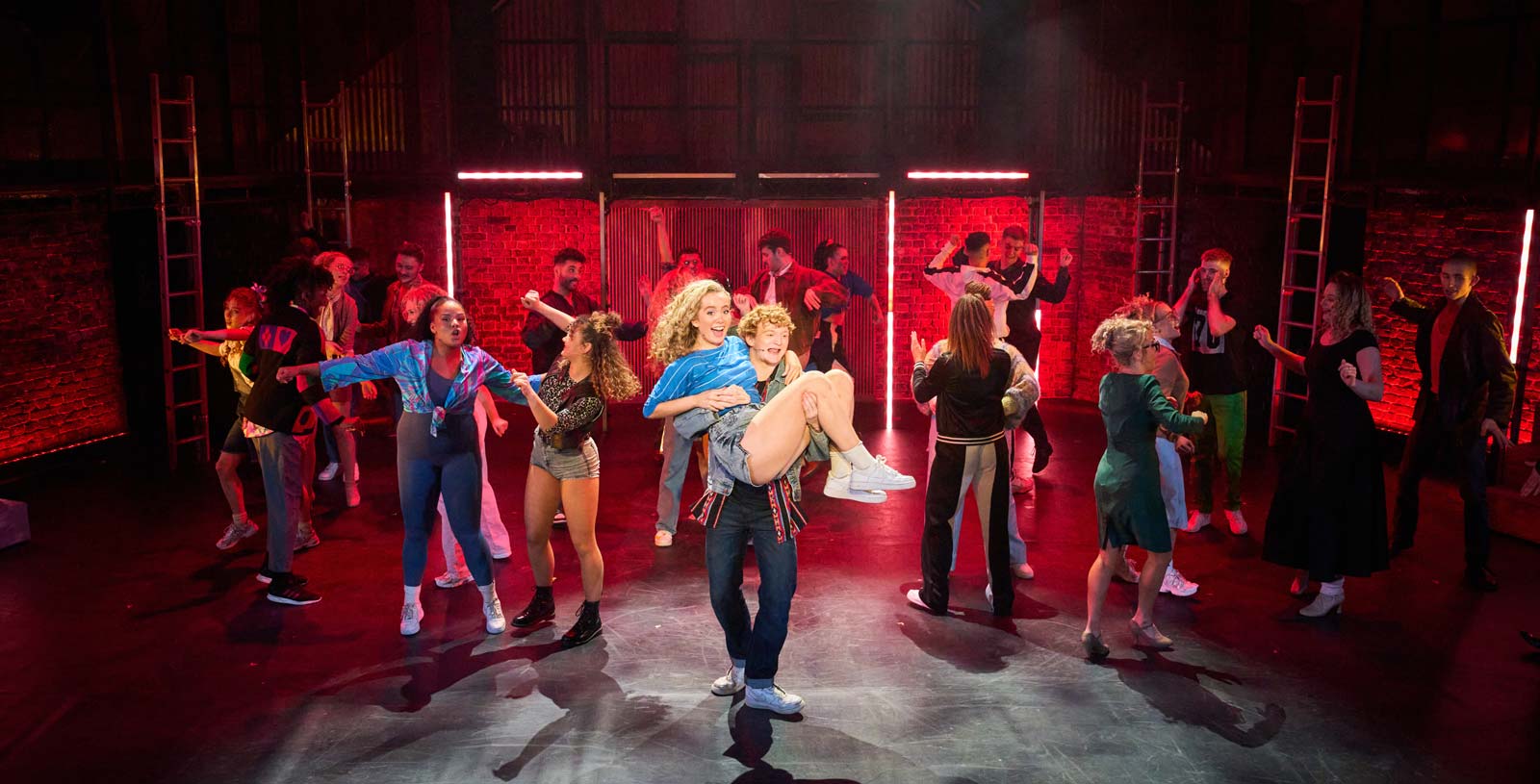 Production of the musical 'Flashdance' with the whole cast on stage dancing against a red neon set