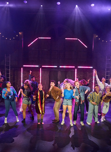 Production of the musical 'Flashdance' with the whole cast on stage dancing against a red neon set